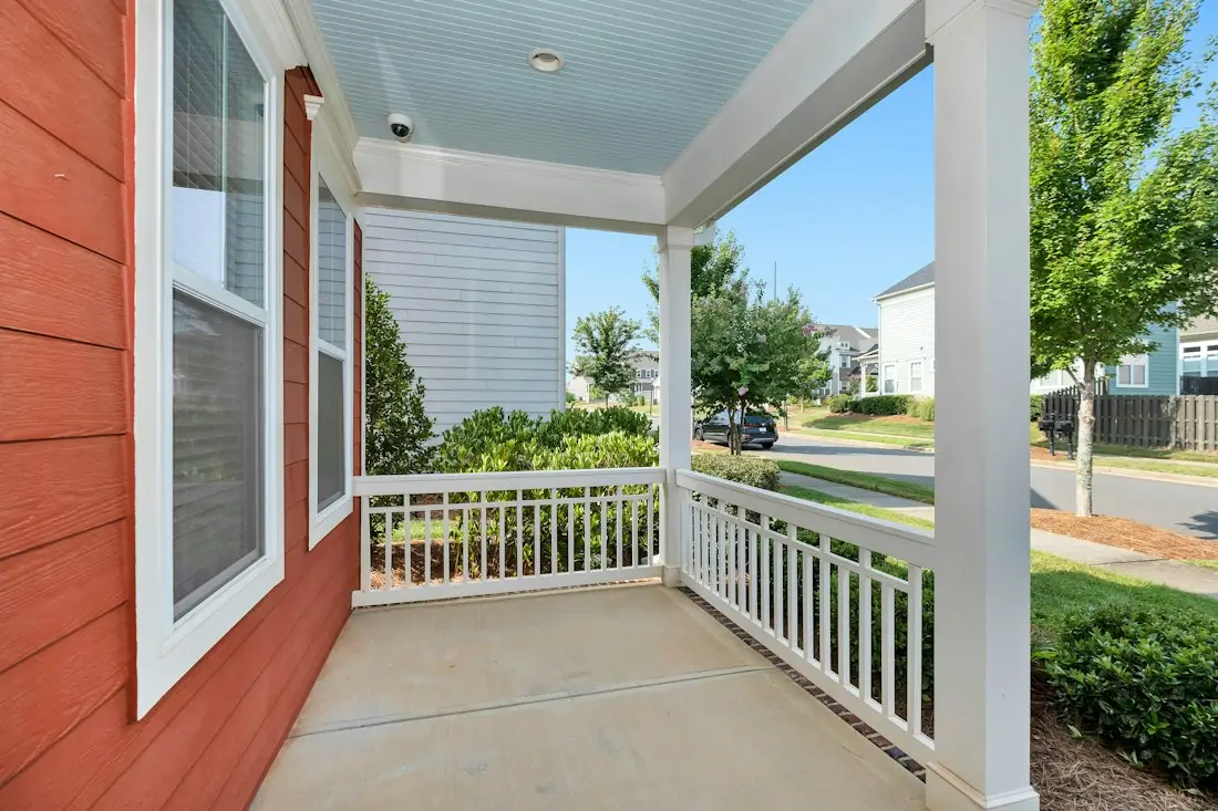 A covered front porch with white railings looking out on a green yard